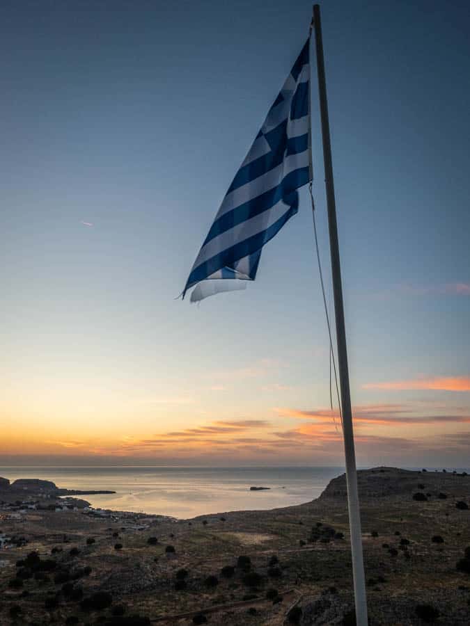 Photo of the Greek flag at sunrise at the Prophet Elias church in Pefkos looking towards Lindos